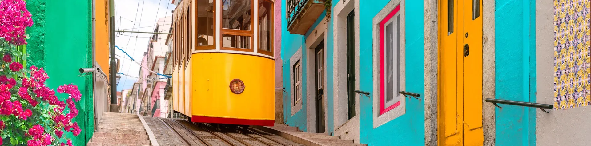 Tram 28 kör uppför en brant gata omgiven av färgglada hus i Lissabon.